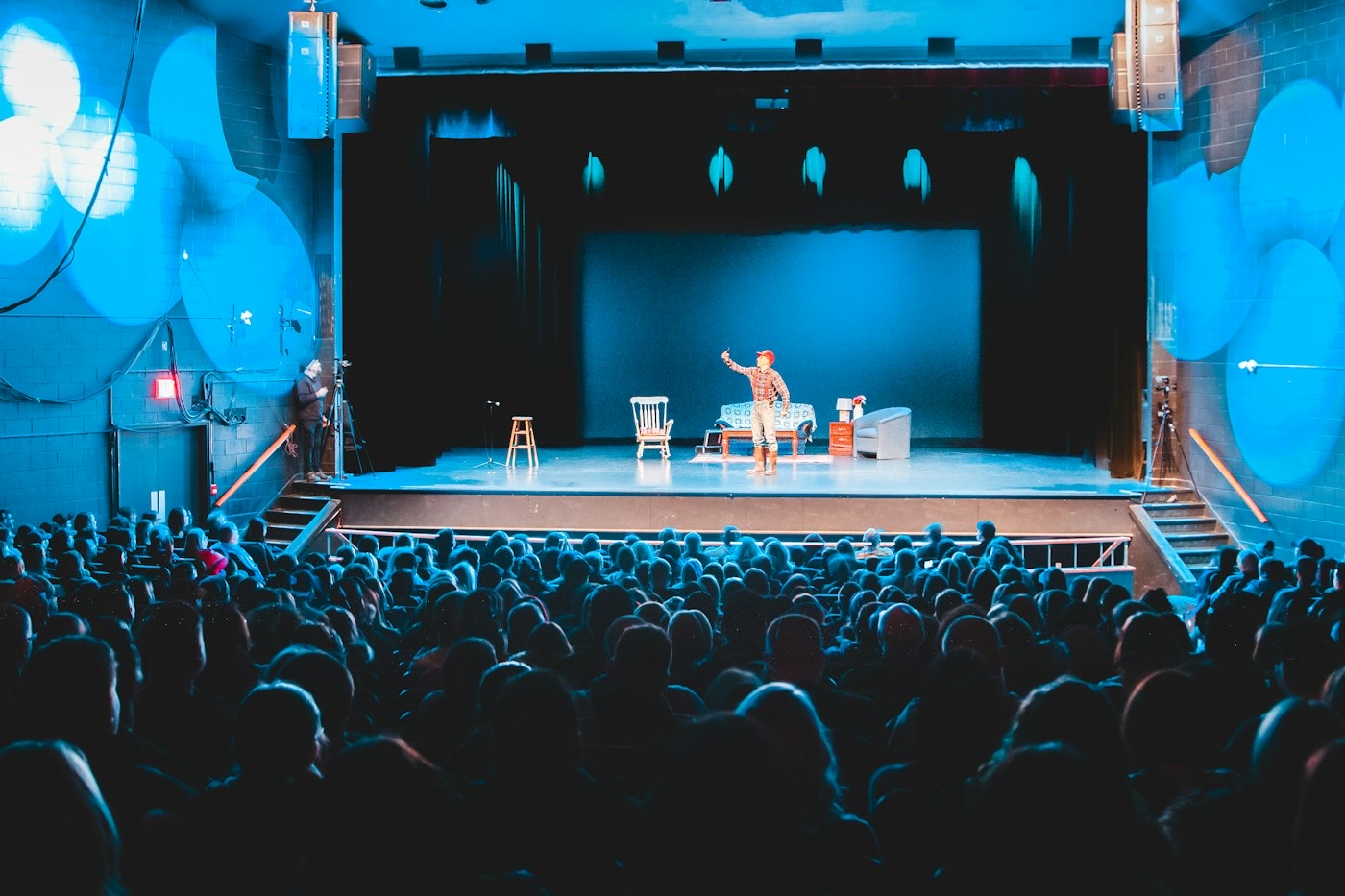Un pequeño teatro lleno, visto desde el público, con una actriz en el escenario